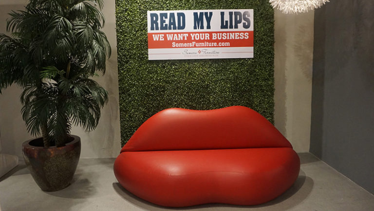 Hedge Back Wall with a tree, logo sign and Red Lip Sofa