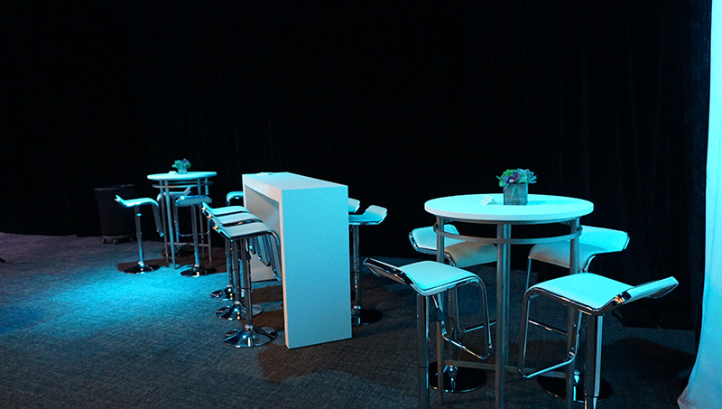 close up of pedestal tables, both round and rectangle with barstools, along with white tables and chairs in the dimly lit event space furnished by Somers Furniture rental division