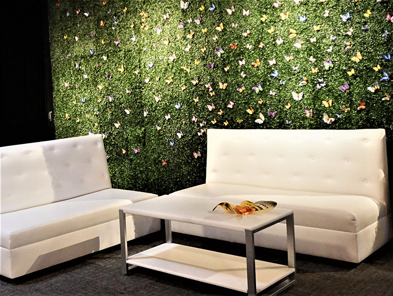 Green hedge with butterflies behind white buttoned sofas and cocktail table in the lounge