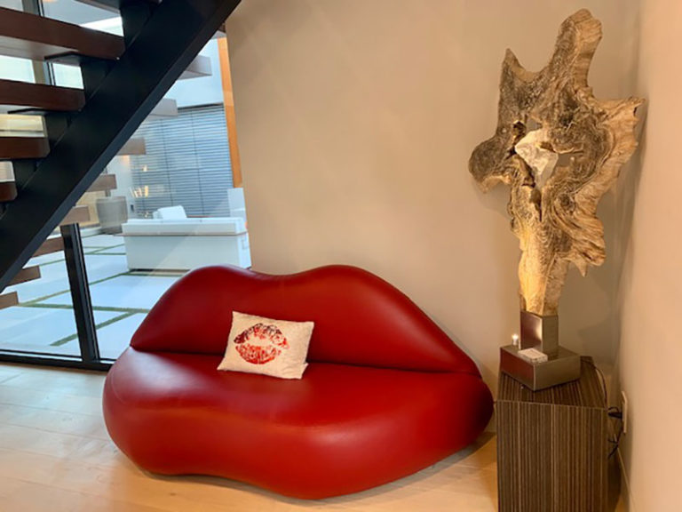 Red Lip Sofa placed in front the staircase and next to a statue in the foyer