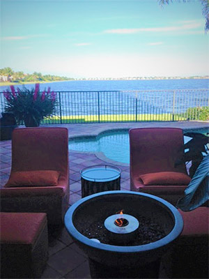 red outdoor patio set and loungers around a fire pit by a pool and lake